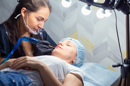 A woman makes permanent lip makeup to another woman in a beauty salon cabinet. Face tattoo. Modern trends in cosmetology