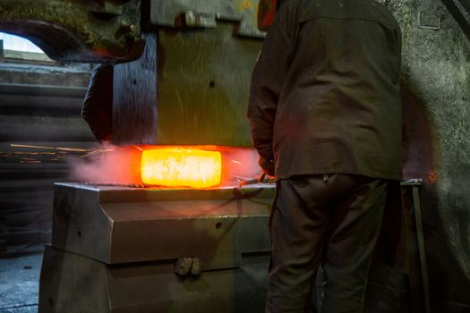close-up picture of hot steel free forging process with big mechanical hammer machine, sparks flying out from workpiece