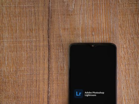Lod, Israel - July 8, 2020: Adobe Lightroom - Photo Editor and Pro Camera app launch screen with logo on the display of a black mobile smartphone on wooden background. Top view flat lay with copy space.