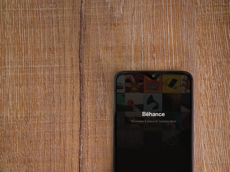 Lod, Israel - July 8, 2020: Adobe Behance app launch screen with logo on the display of a black mobile smartphone on wooden background. Top view flat lay with copy space. 