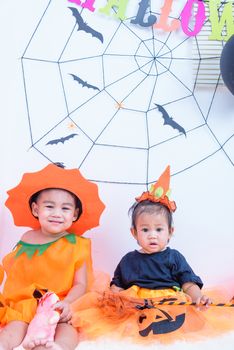 Funny happy brethren baby girl and kid boy in Halloween costume with pumpkin Jack with Cobweb on background