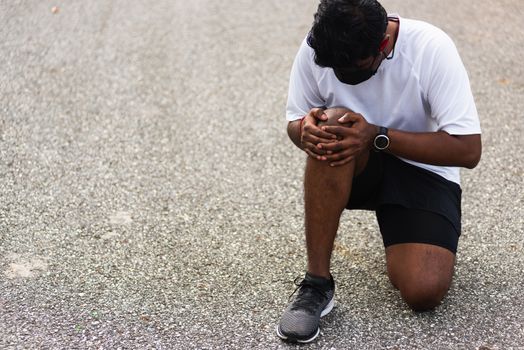 Close up Asian young sport runner black man wear watch sitting hands joint hold knee pain during the run while running at the outdoor street health park, healthy exercise injury from workout concept