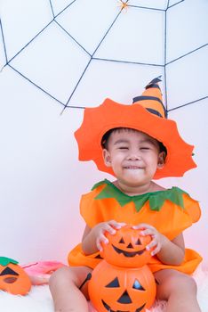 Funny happy kid in Halloween costume with pumpkin Jack with Cobweb on background