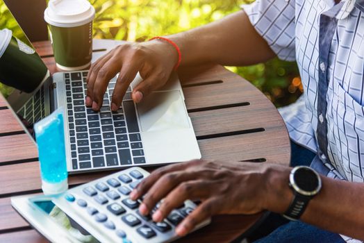 Happy Asian black businessman person or office worker wear face mask protect sitting on desk work from home using laptop computer typing keyboard and connect networking online at the coffee cafe shop