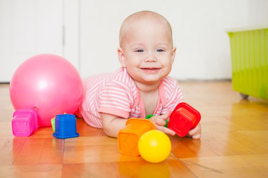 Little baby girl sitting on the floor, crawling and playing with brightly colored educational toys, pyramids