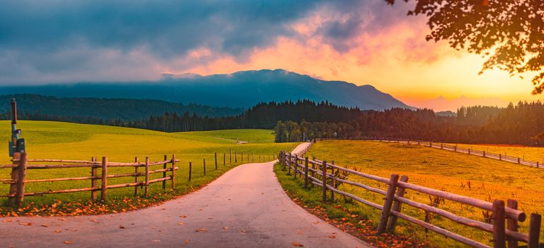 Panorama of rural road in countyside of Bavaria, Germany. Green meadow and pathway in foreground with dramatic sunset sky and clouds in background