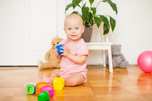 Little baby girl sitting on the floor, crawling and playing with brightly colored educational toys, pyramids