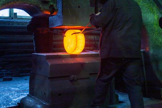 close-up picture of hot steel free forging process with big mechanical hammer machine, sparks flying out from workpiece