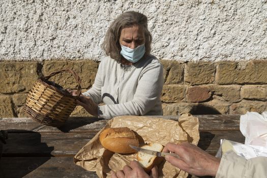 A senior adult woman, wearing a face mask, chooses the amount of bread she wants, before eating at the mountain hut of the fountain of Artica, in Luesia, Spain.