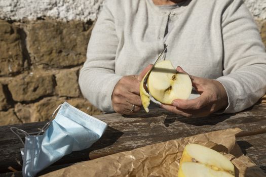 A senior woman, peel half an apple to eat at the mountain hut of the fountain of Artica, in Luesia, Spain.