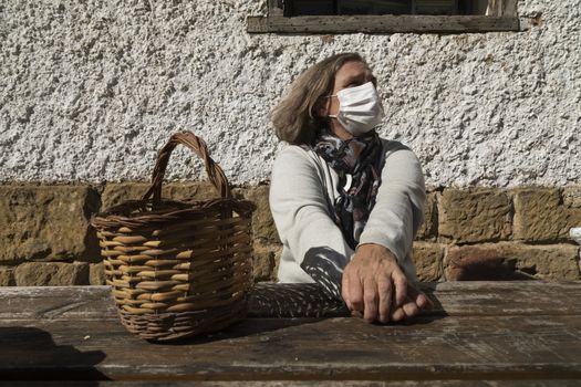 A senior woman, wearing a white protective face mask, stretches her arms and relaxes, near the mountain hut of the fountain of Artica, in Luesia, Spain.