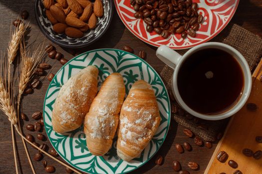 breakfast with breads and coffee on wooden table with coffee beans and almonds under daylight in plane