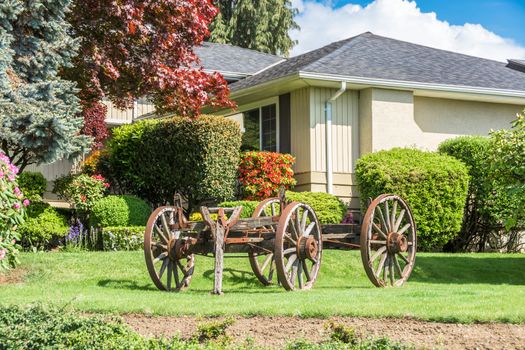 Front yard in residential community creatively landscaped with old horse vehicle on green lawn