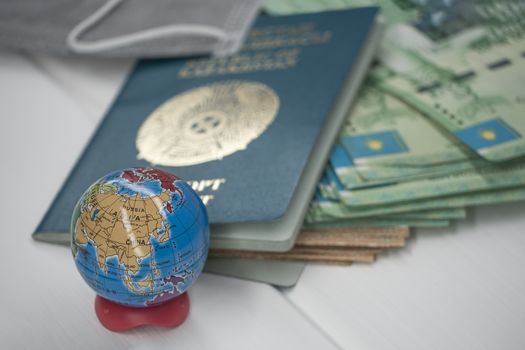 Quarantine in Kazakhstan. Tenge money with medical face masks, a globe, a card and a passport are on the table. The closure of borders and travel in Kazakhstan.