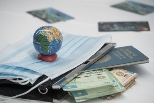 Quarantine in Kazakhstan. Tenge money with medical face masks, a globe, a card and a passport are on the table. The closure of borders and travel in Kazakhstan.