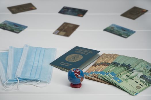 Quarantine in Kazakhstan. Tenge money with medical face masks, a globe, a card and a passport are on the table. The closure of borders and travel in Kazakhstan.