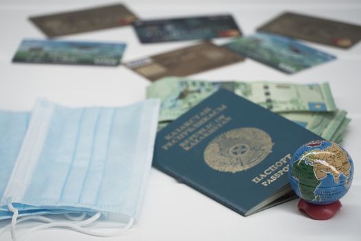 Quarantine in Kazakhstan. Tenge money with medical face masks, a globe, a card and a passport are on the table. The closure of borders and travel in Kazakhstan.