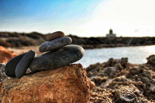 Rocks stacked on the shore. Tabarca island lighthouse in the background.