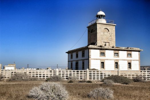 Lighthouse of Tabarca Island, Spain, surrounded by vegetation under blue sky in summer