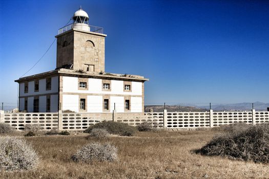 Lighthouse of Tabarca Island, Spain, surrounded by vegetation under blue sky in summer