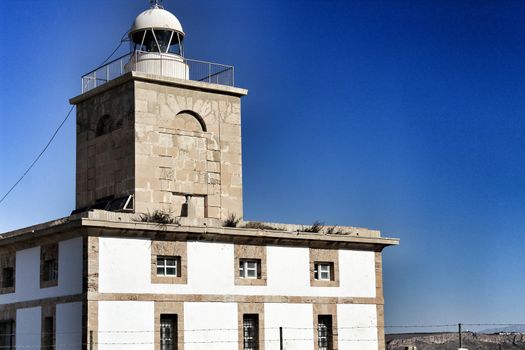 Lighthouse of Tabarca Island, Spain, surrounded by vegetation under blue sky in summer