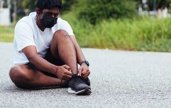 Close up Asian sport runner black man wear face mask protective he shoelace trying running shoes getting ready for jogging and run at the outdoor street, health exercise workout concept