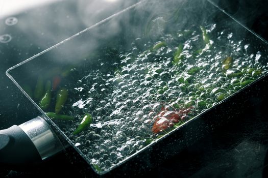 boiling water with chili pepper in pan on electric stove in kitchen, hot water with bubbles and steam