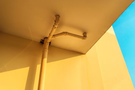 sewer pipes or drain pipes on yellow building wall with beautiful blue sky