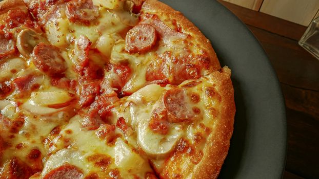 The pizza in black plate on wood table for food content.
