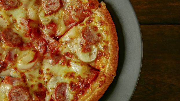 The pizza in black plate on wood table for food content.
