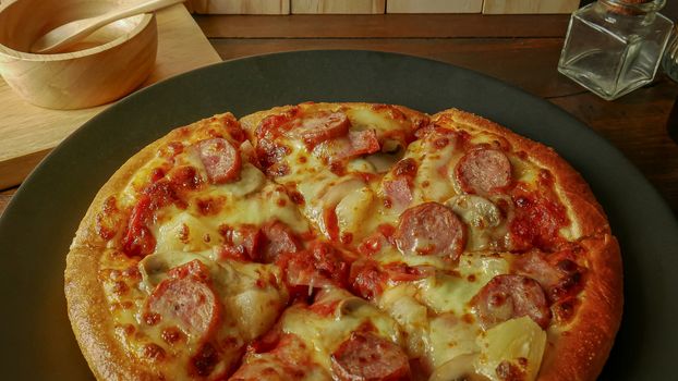 The pizza in black plate on wood table for food content.
