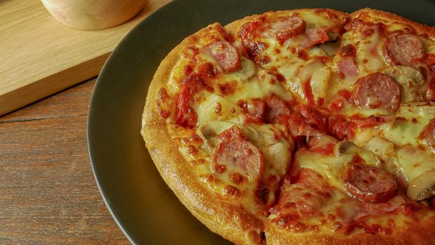 The pizza in black plate on wood table for food content.
