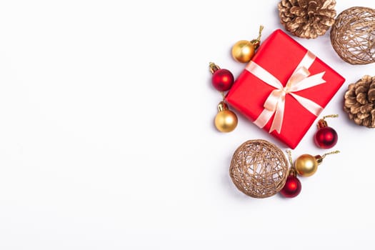 Christmas composition. Red gift box, pine cones, gold and red ornament decorations on white background. Winter holidays concept. Top view copy space