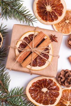 Christmas composition with handmade kraft paper gift box, dried citrus slices, cinnamon, anise, pine cones and fir tree branches, top view close up