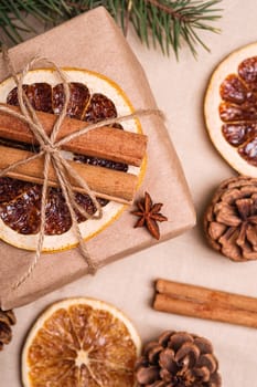 Christmas composition with handmade kraft paper gift box, dried citrus slices, cinnamon, anise, pine cones and fir tree branches, top view macro