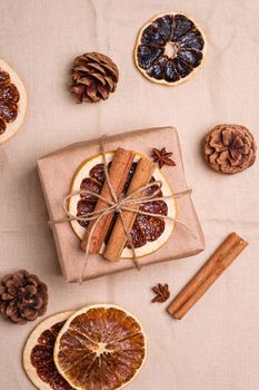 Christmas composition with handmade kraft paper gift box, dried citrus slices, cinnamon, anise, pine cones, top view close up