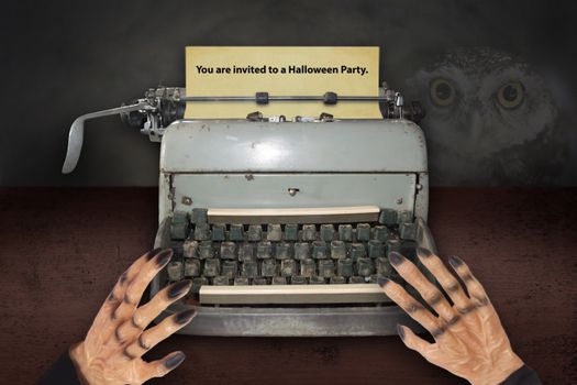 Devil's hand typing invitations for Halloween with old typewriter.