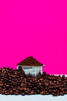 Coffee beans and portafilter with ground coffee in a composition on a pink background.