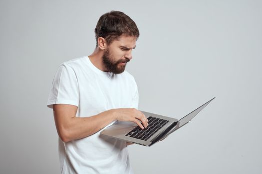 A man with a laptop in his hands on a light background in a white t-shirt emotions light background cropped view model portrait new technologies. High quality photo