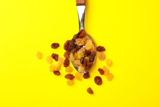 Spoon with raisins on yellow background, top view