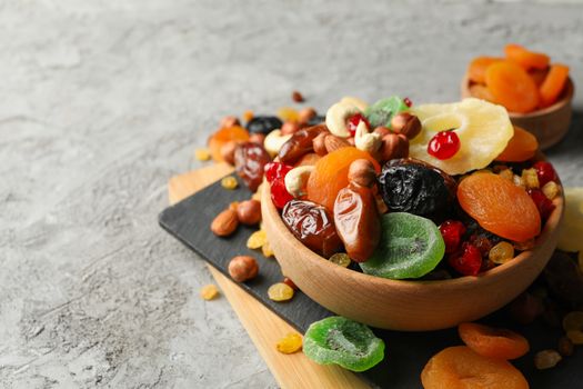 Board and bowls with dried fruits and nuts on gray background