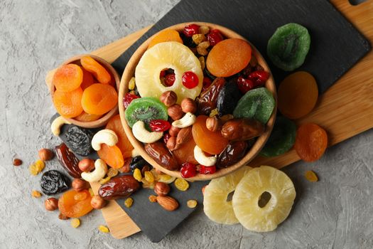 Board and bowls with dried fruits and nuts on gray background