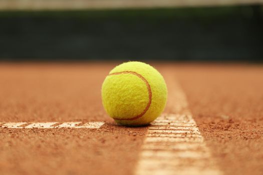 Light green tennis ball on clay court, close up
