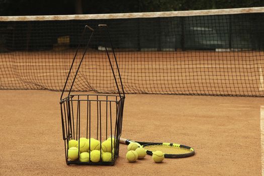 Racket and basket with balls on clay court
