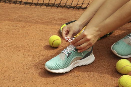 Woman tying shoelaces on clay court with racket and tennis balls