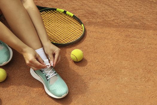 Woman tying shoelaces on clay court with racket and tennis balls