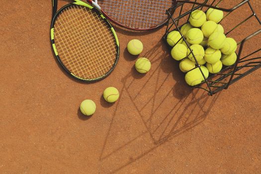 Rackets and basket with tennis balls on clay court