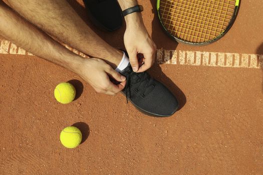 Man ties his shoelaces on clay court with racket and balls