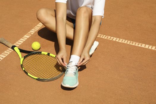 Woman ties shoelace on clay court with racket and and ball