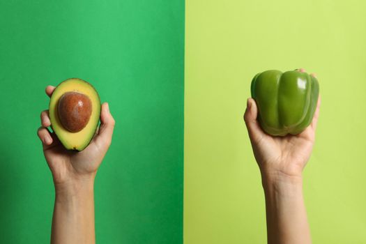 Female hands hold pepper and avocado on two tone background